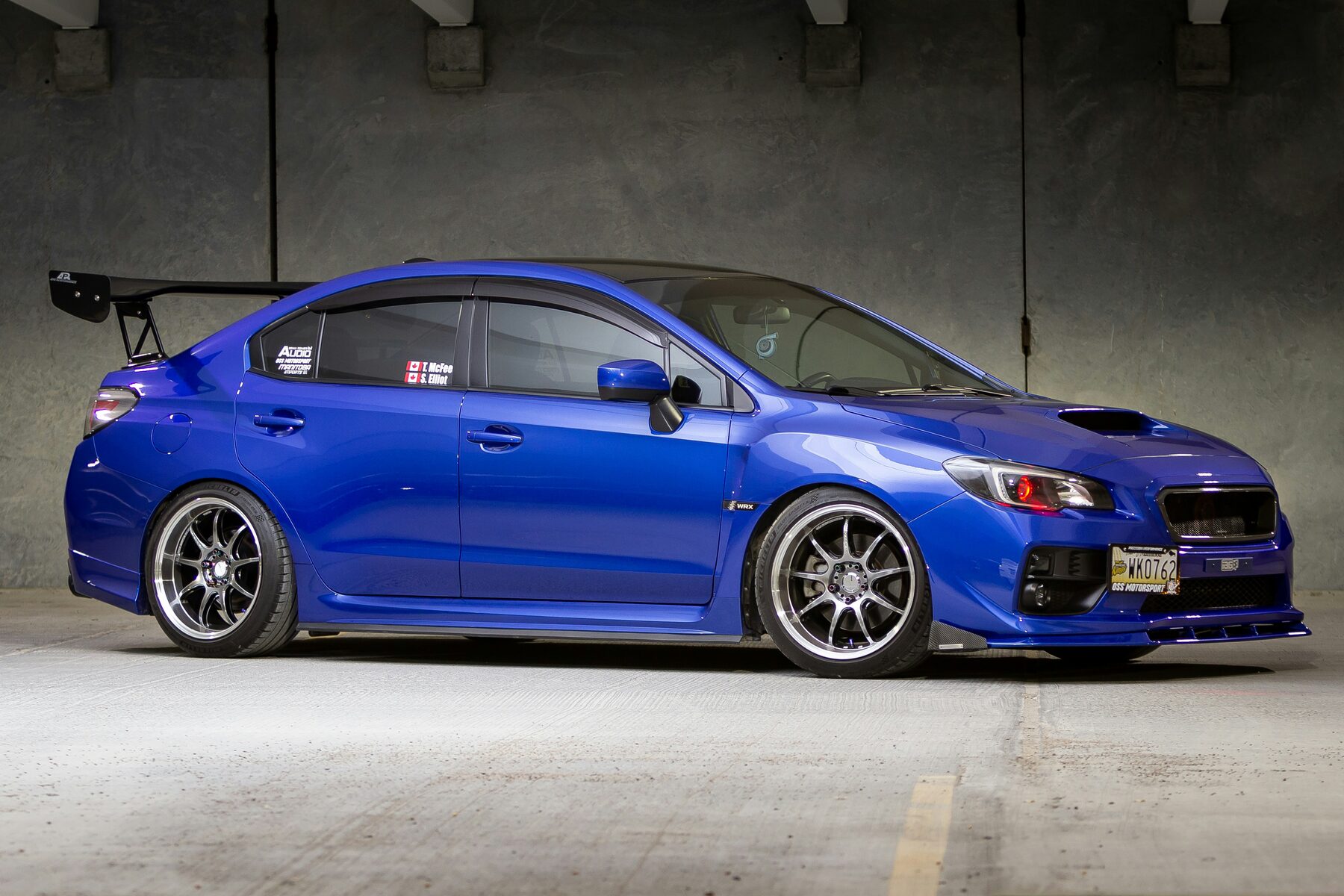 Blue lowered Subaru WRX with aftermarket wheels in a garage