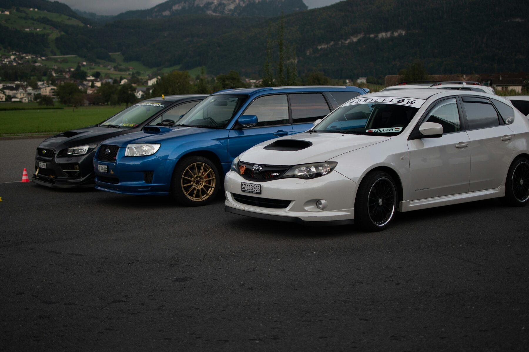 Three Subaru WRX cars parked in front of a mountain landscape